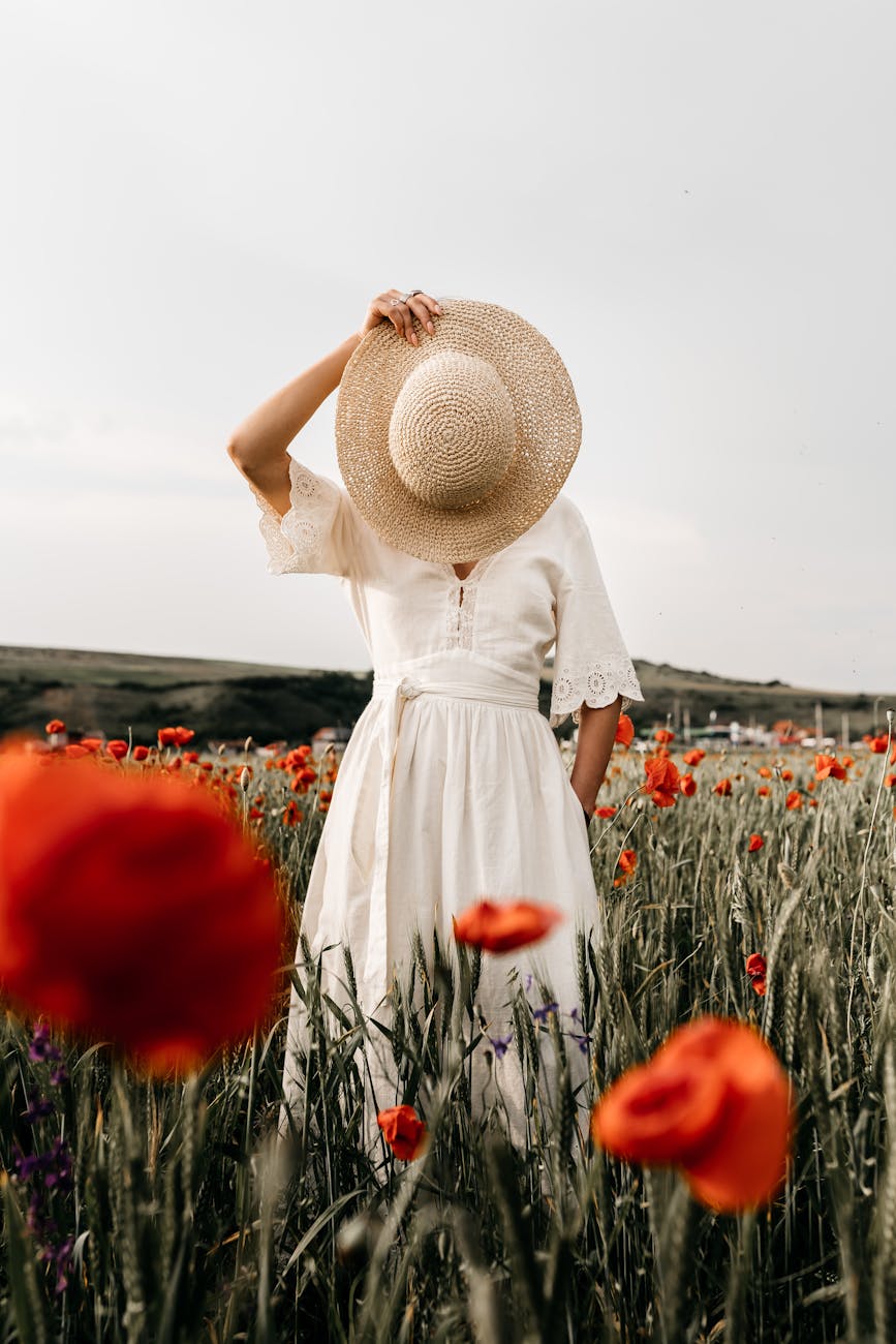 unrecognizable woman with hat standing in meadow with flowers